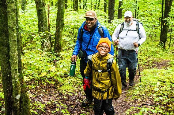 smiling boy and two adults hiking in woods