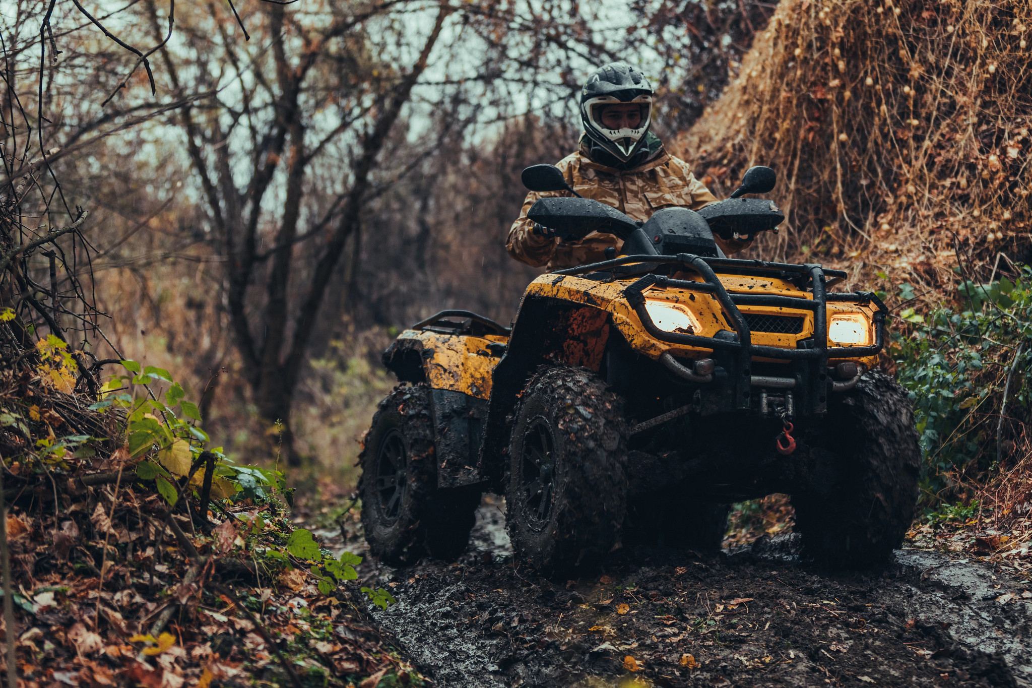 A person rides an ATV on a muddy trail. 