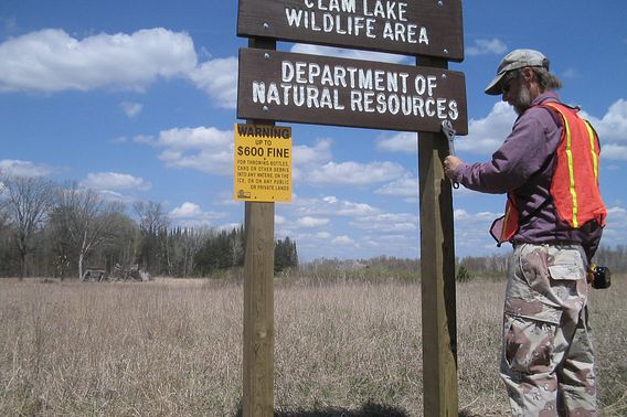 A DNR employee performs maintenance on a wooden sign at the Clam Lake Wildlife Area.