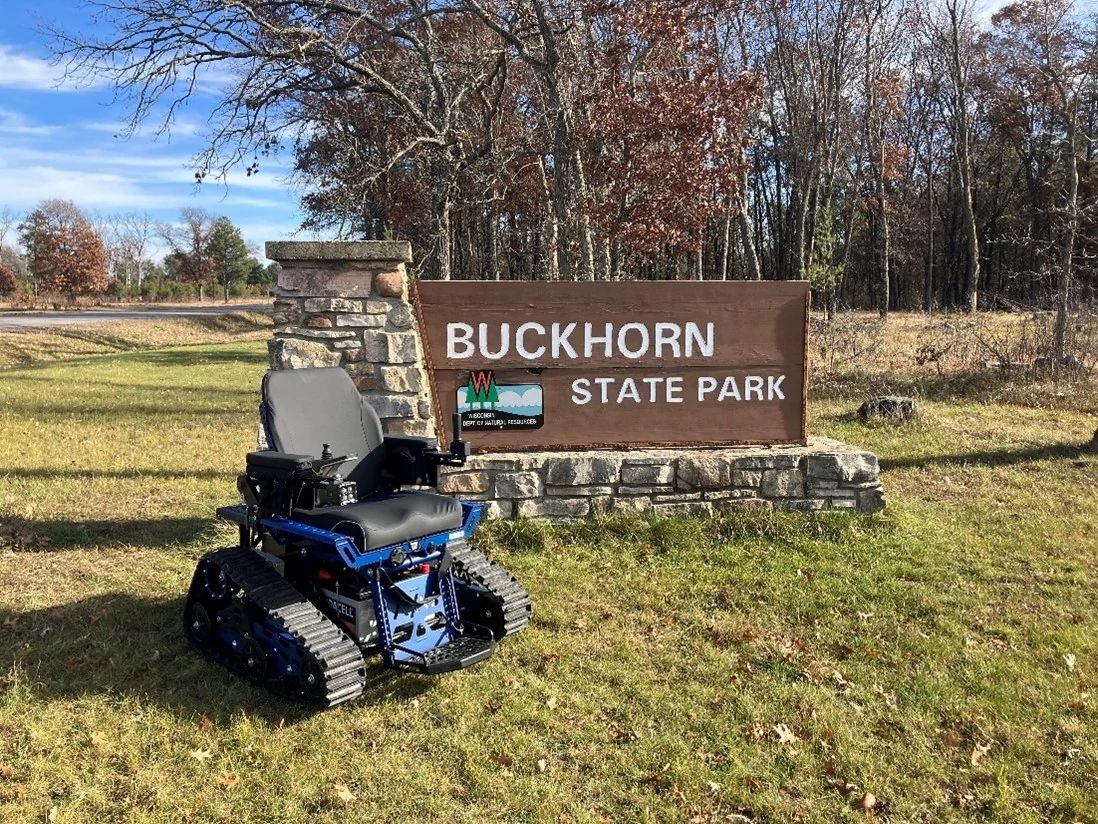 A photo of a Buckhorn Wheelchair in front of the Buckhorn State Park sign.