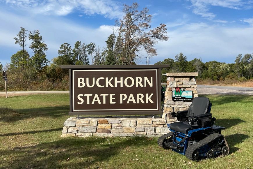 A photo of a Track Wheelchair in front of the Buckhorn State Park sign.