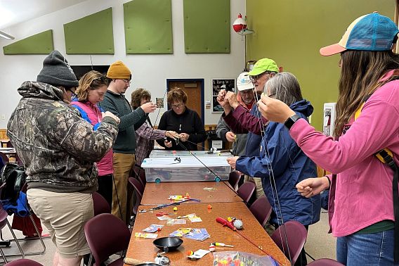 Several people standing around a table as they learn to tie fishing knots and use basic equipment.