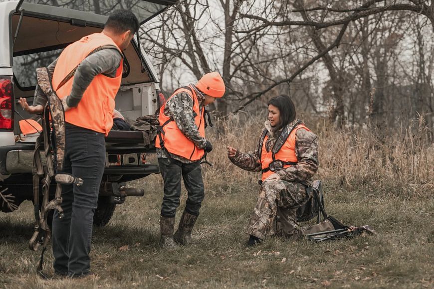 Family members wearing blaze orange prepare for a hunt in autumn woods