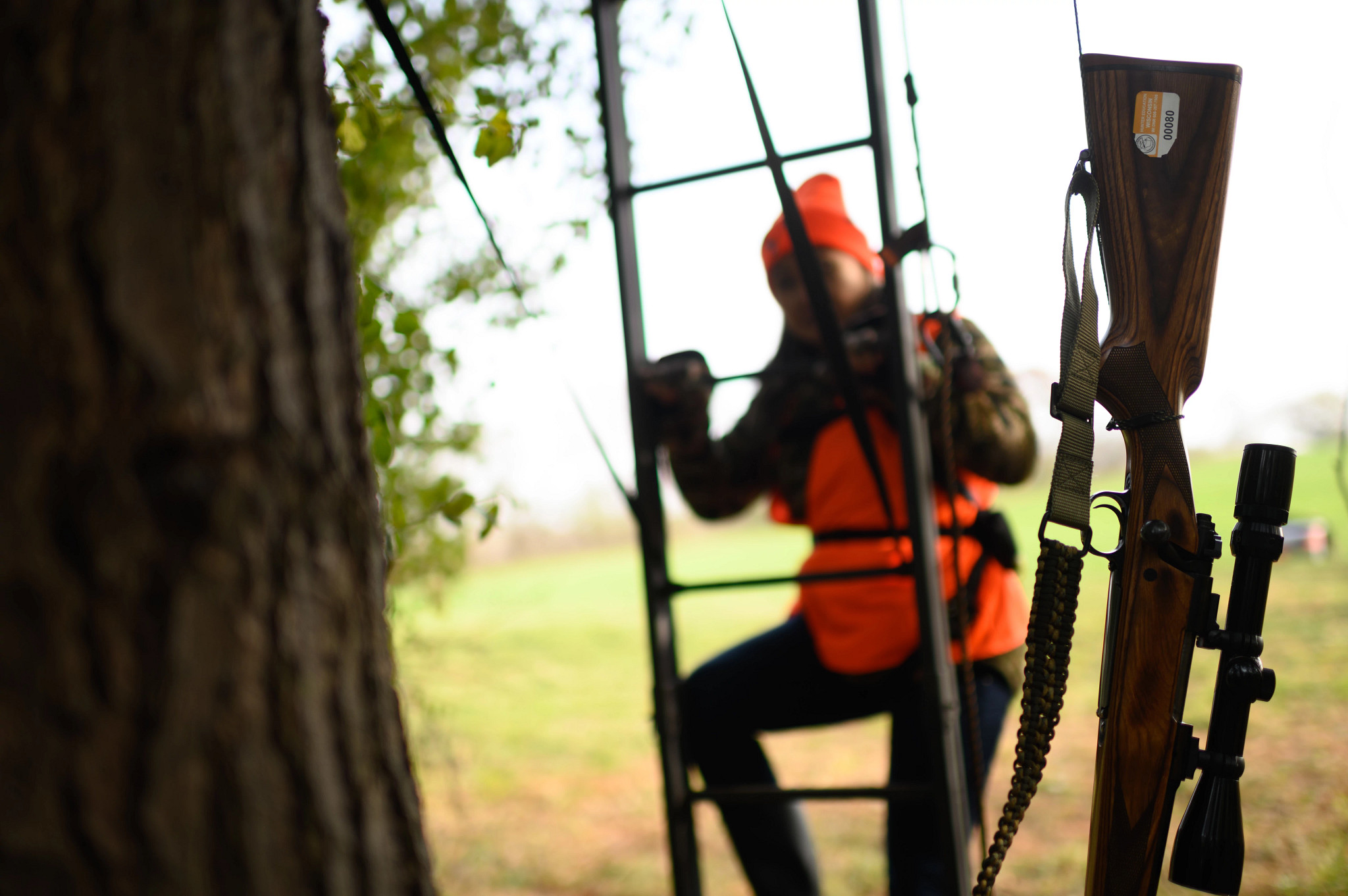 woman climbing tree stand using a pulley for her rifle