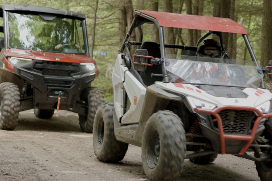 Two UTVs ride on a trail; the one in front is a child-sized model.