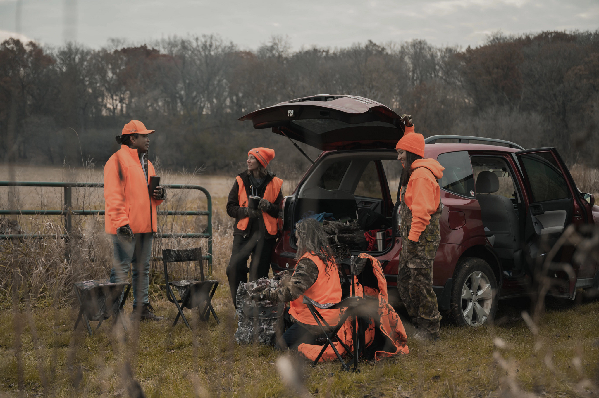 group of four male and female hunters wearing blaze orange talking in a circle in a field