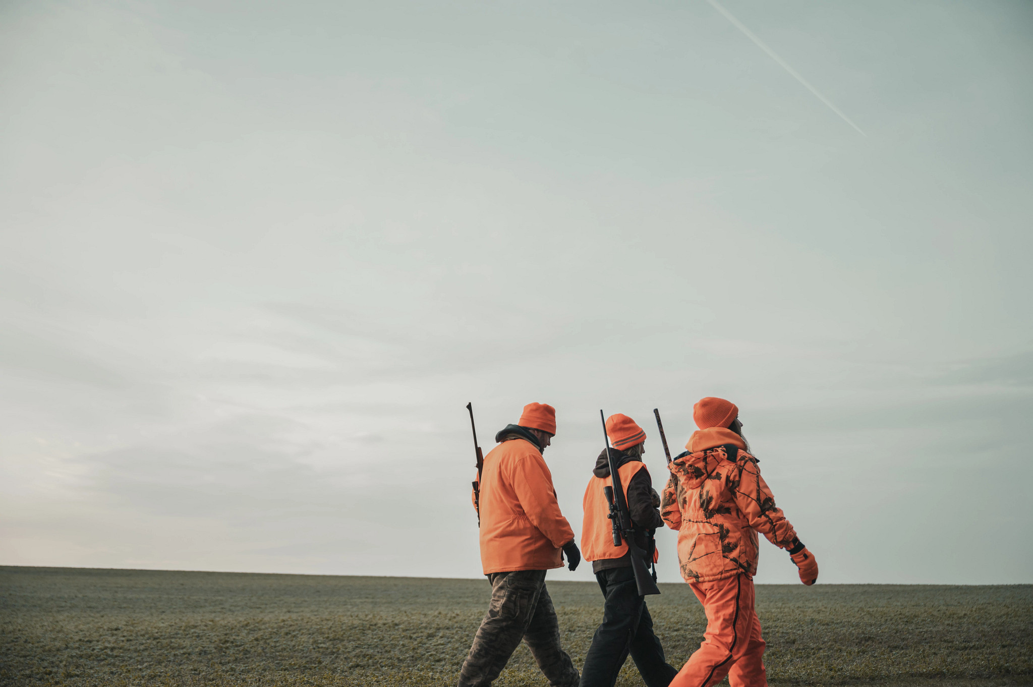 group of three hunters wearing blaze orange walking across field