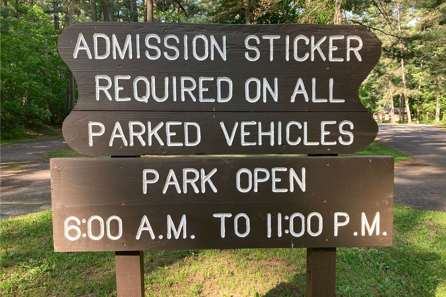 a wooden sign that says admission sticker required on all parked vehicles park open 6 a.m. - 11 p.m.