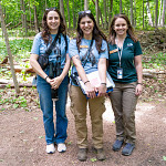 Three people stand smiling in a forest.