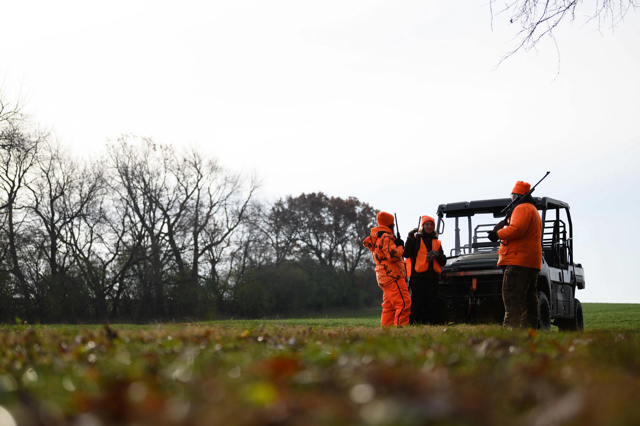 group of 3 hunters wearing blaze orange stand around talking next to a UTV
