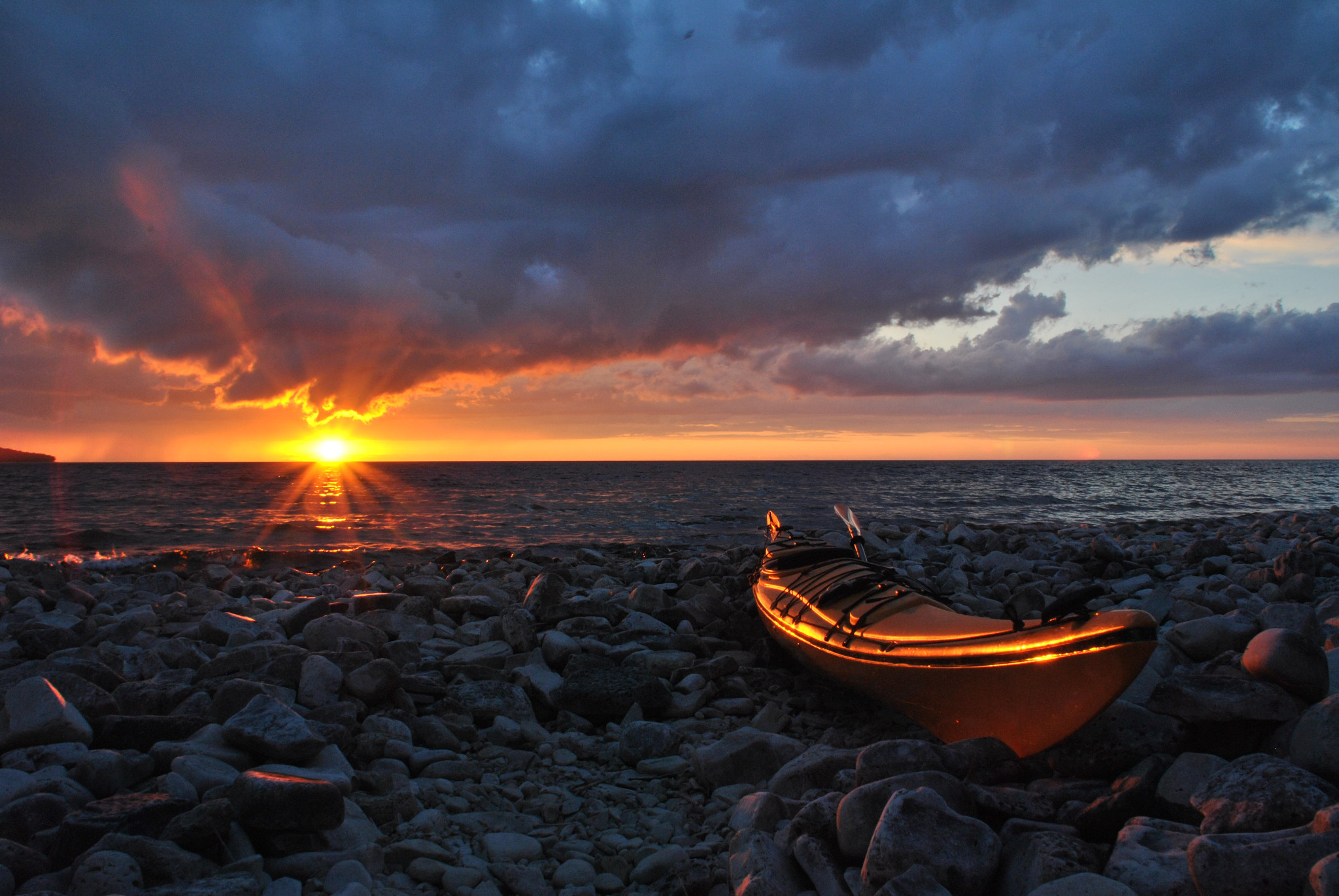 the sun sets on the rocky shoreline of lake Michigan with a kayak just shored on the beach.