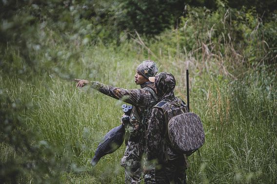Two people dressed in hunting gear in the middle of a grassy area.