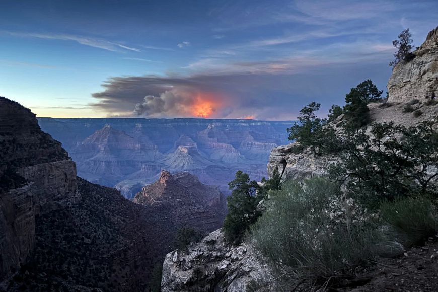 A fire burns on the far side of a large canyon, the smoke filling the sky in the distance.