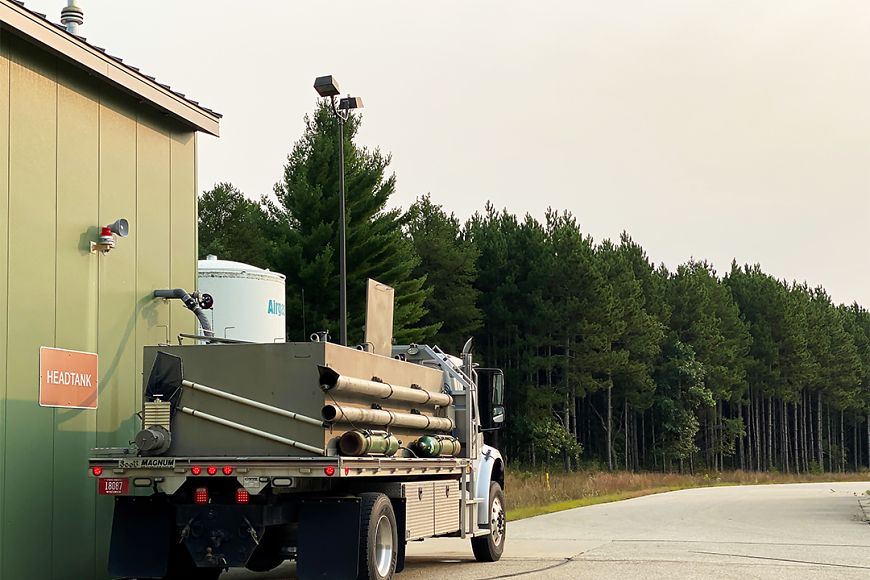 A fish stocking truck sits parked next to a beige building with a sign reading "Headtank."