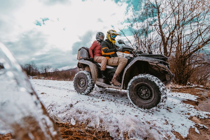 Two ATV riders wearing helmets navigate a snowy trail. 