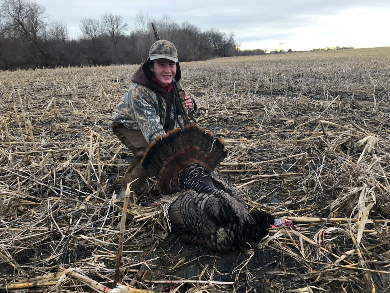 young boy wearing camo posing with harvested turkey