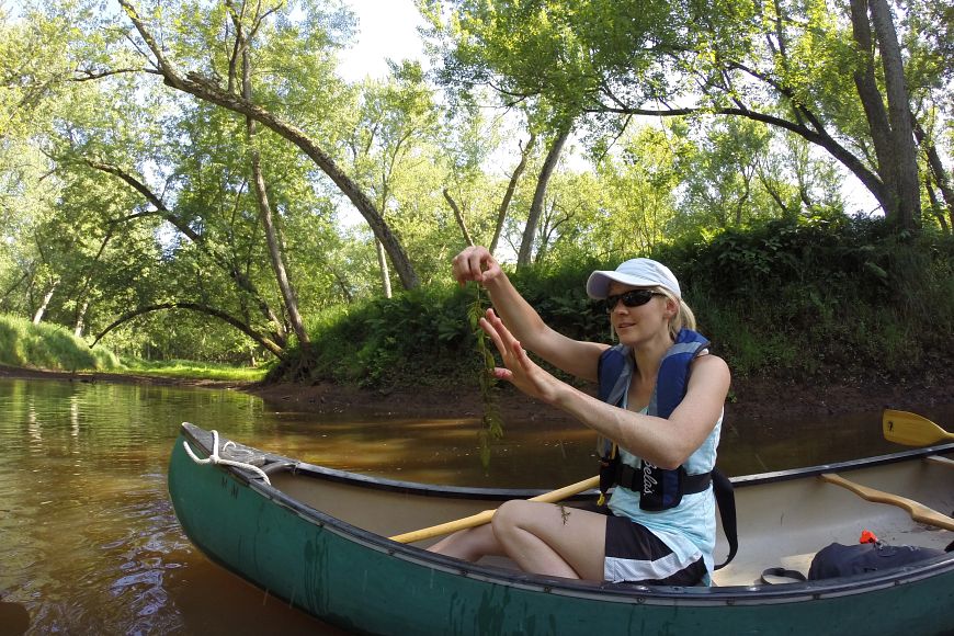 A woman in a canoe on a river, holding up an aquatic invasive species.