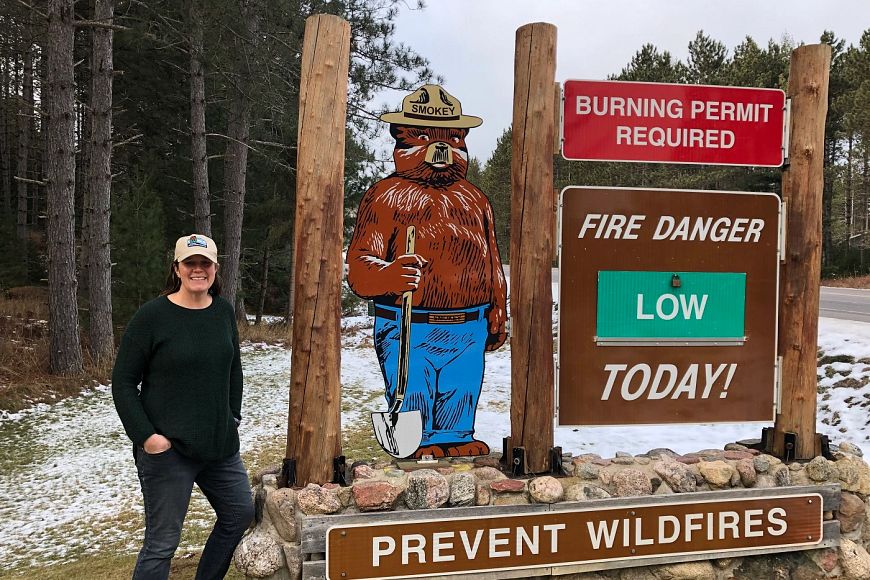 Heather Berklund stands near a sign featuring Smokey Bear