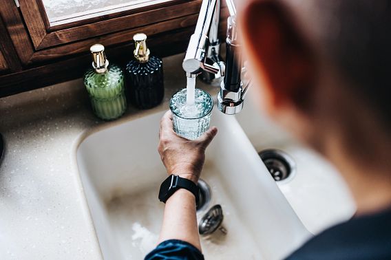 An over the shoulder view of a man filling a glass of filtered water right from the tap in the kitchen at home.