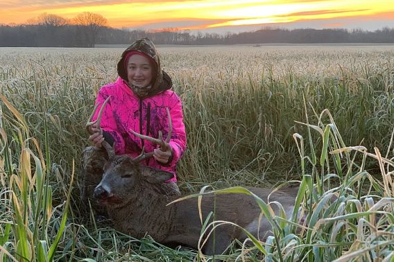 young girl at sunrise with first harvested buck